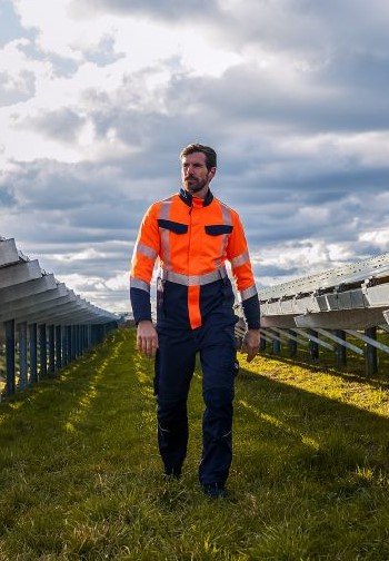 Ein Mann läuft durch eine Solaranlage und trägt eine Multinorm Warnschutz Hose.